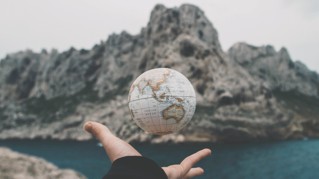 Fotografija ruke koja hvata mali globus ispred planina i mora
